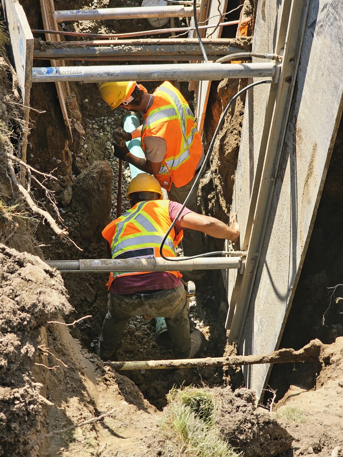 Workers coordinating utility installation within a shored excavation